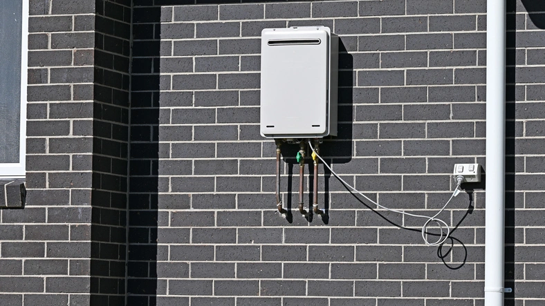 A white Tankless water Heater mounted on a textured brick wall.